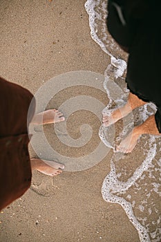 Hipster couple standing walking barefoot on beach, top view. Feet in water foam, summer vacation