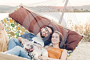 Hipster couple on a trip to the beach, young freelancer man relaxing in a hammock with his woman, romantic couple on vacation with
