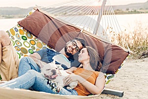 Hipster couple on a trip to the beach, young freelancer man relaxing in a hammock with his woman, romantic couple on vacation with