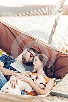 Hipster couple on a trip to the beach, young freelancer man relaxing in a hammock with his woman, romantic couple on vacation with