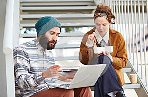 Hipster couple using computer and eating lunch outdoors