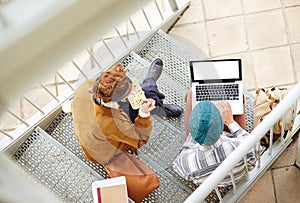 Hipster couple using computer and eating lunch outdoors