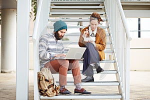 Hipster couple using computer and eating lunch outdoors