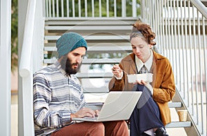 Hipster couple using computer and eating lunch outdoors