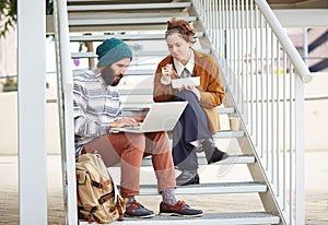 Hipster couple using computer and eating lunch outdoors