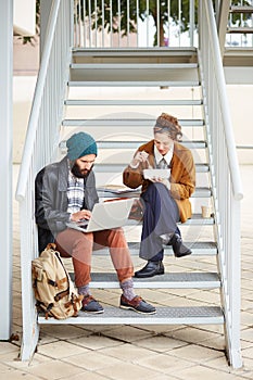 Hipster couple using computer and eating lunch outdoors