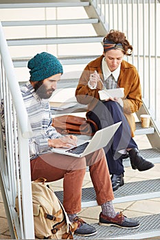 Hipster couple using computer and eating lunch outdoors