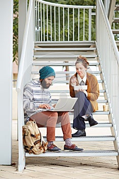 Hipster couple using computer and eating lunch outdoors