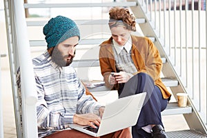 Hipster couple using computer and smartphone outdoors