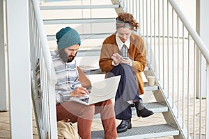 Hipster couple using computer and smartphone outdoors