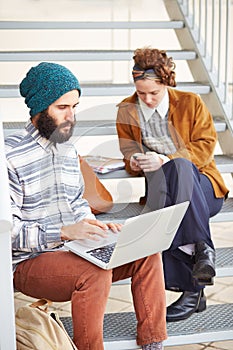 Hipster couple using computer and smartphone outdoors