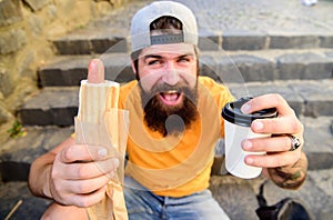 Hipster eat hot dog and drink coffee. Lunch time concept. Hipster enjoy hot dog and drink paper cup beverage. Fast food