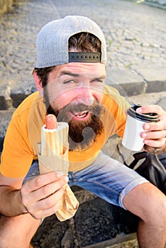 Hipster enjoy hot dog and drink paper cup. Man bearded enjoy street food urban background. Take break to have snack
