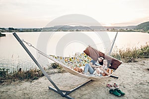 Hipster family on vacation concept, happy woman and man relaxing on a hammock at the beach with their cute bulldog pet, couple