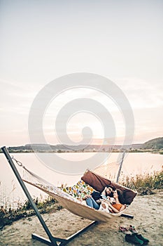 Hipster family on vacation concept, happy woman and man relaxing on a hammock at the beach with their cute bulldog pet, couple