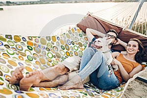 Hipster family on vacation concept, happy woman and man relaxing on a hammock at the beach with their cute bulldog pet, couple