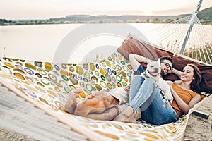 Hipster family on vacation concept, happy woman and man relaxing on a hammock at the beach with their cute bulldog pet, couple