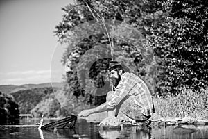 Hipster fishing with spoon-bait. mature bearded man with fish on rod. successful fisherman in lake water. fly fish hobby