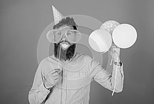 Hipster in giant sunglasses celebrating. Guy in party hat with air balloons celebrates. Man with beard on cheerful face