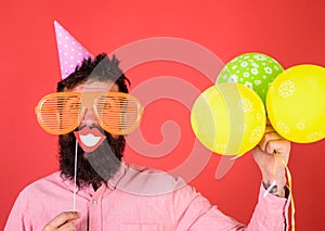 Hipster in giant sunglasses celebrating. Guy in party hat with air balloons celebrates. Photo booth fun concept. Man