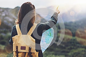 Hipster girl with backpack enjoying sunset on peak of foggy mountain, looking a map and poining hand. Tourist traveler on back