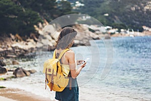 Hipster girl with backpack hold on smart phone gadget in sand coastline, mock up. Traveler using in female hand mobile on back