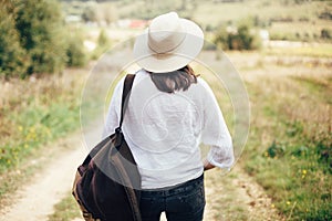 Hipster girl with backpack traveling and walking on top of sunny mountain and looking at hills and woods. Stylish woman in hat