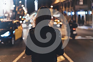 Hipster girl in black leather jacket from back on background illumination glow bokeh light in night atmospheric christmas city