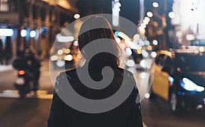 Hipster girl in black leather jacket from back on background illumination glow bokeh light in night atmospheric christmas city, hi