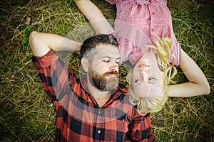 Hipster and girl enjoy summer day on nature. Couple in love relax on green grass. Bearded man and woman with long blond