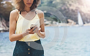 Hipster girl hold on smart phone gadget in sand coastline, mock up blank screen. Traveler using in female hand mobile