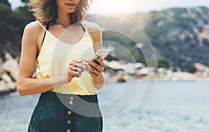 Hipster girl hold on smart phone gadget in sand coastline, mock up blank screen. Traveler using in female hand mobile