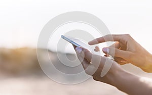 Hipster girl hold on smart phone gadget in sand coastline, mock up blank screen. Traveler using in female hand mobile