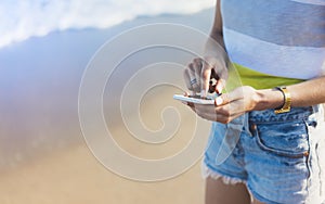 Hipster girl hold on smart phone gadget in sand coastline, mock up of blank screen. Traveler using in female hand mobile