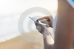 Hipster girl hold on smart phone gadget in sand coastline, mock up blank screen. Traveler using in female hand mobile