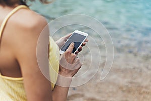Hipster girl hold on smart phone gadget in sand coastline, mock up blank screen. Traveler using in female hand mobile