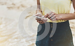 Hipster girl hold on smart phone gadget in sand coastline, mock up blank screen. Traveler using in female hand mobile on back