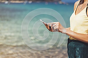 Hipster girl hold on smart phone gadget in sand coastline, mock up blank screen. Traveler using in female hand mobile on back