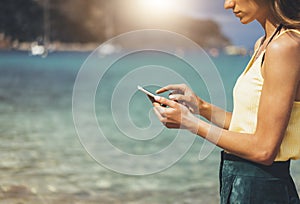Hipster girl hold on smart phone gadget in sand coastline, mock up blank screen. Traveler using in female hand mobile on back