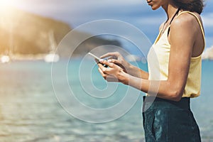 Hipster girl hold on smart phone gadget in sand coastline, mock up blank screen. Traveler using in female hand mobile on back