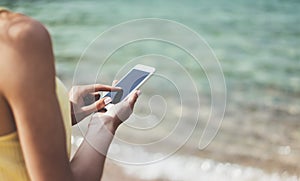 Hipster girl hold on smart phone gadget in sand coastline, mock up blank screen. Traveler using in female hand mobile on back