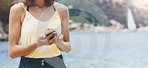 Hipster girl hold on smart phone gadget in sand coastline, mock up blank screen. Traveler using in female hand mobile on back