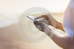 Hipster girl hold on smart phone gadget in sand coastline, mock up blank screen. Traveler using in female hand mobile on backg