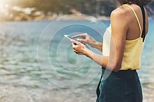 Hipster girl hold on smart phone gadget in sand coastline, mock up blank screen. Traveler using in female hand mobile on backgroun