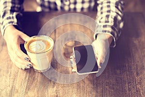 Hipster girl holding a coffee and cell phone on wooden table