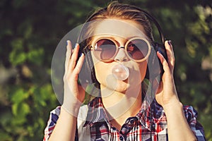 Hipster girl listening to music on headphones and chews the cud.