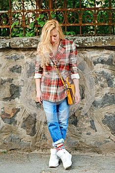 Hipster girl with long blonde hair wearing trendy plaid jacket posing at street. Urban clothing style