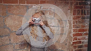 Hipster girl making photography on vintage camera on brick wall background. Young girl using retro photo camera in photo