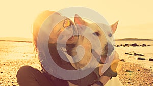 Hipster girl playing with dog at a beach during sunset