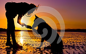 Hipster girl playing with dog at a beach during sunset, silhouettes